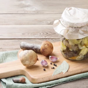 Pilze, Knoblauch, Pfeffer und Lorbeer sowie ein Glas mit eingelegten Porcini auf einem Holzbrett