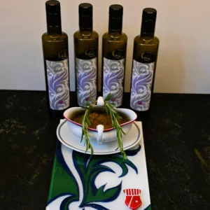 Im Hintergrund sieht man 4 Avistria Olivenölflaschen, davor steht eine Keramikschale gefüllt mit Preporuka Maslinara auf einer Glasfliese im Avistria Design