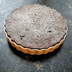 Auf einer dunklenen steineren Arbeitsplatte steht ein Teller mit einer gebackene Chocolata mit Puderzucker garniert